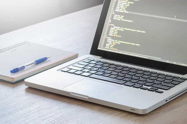 A laptop displaying code on a desk next to a notepad