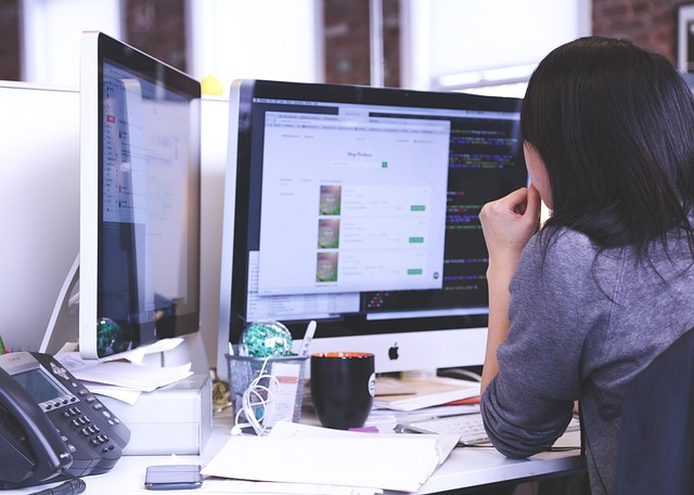 A woman sitting at a desk working on dual computer monitors